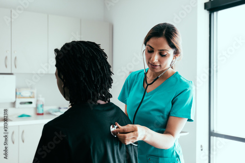 Female patient sitting while nurse holds stethoscope to chest