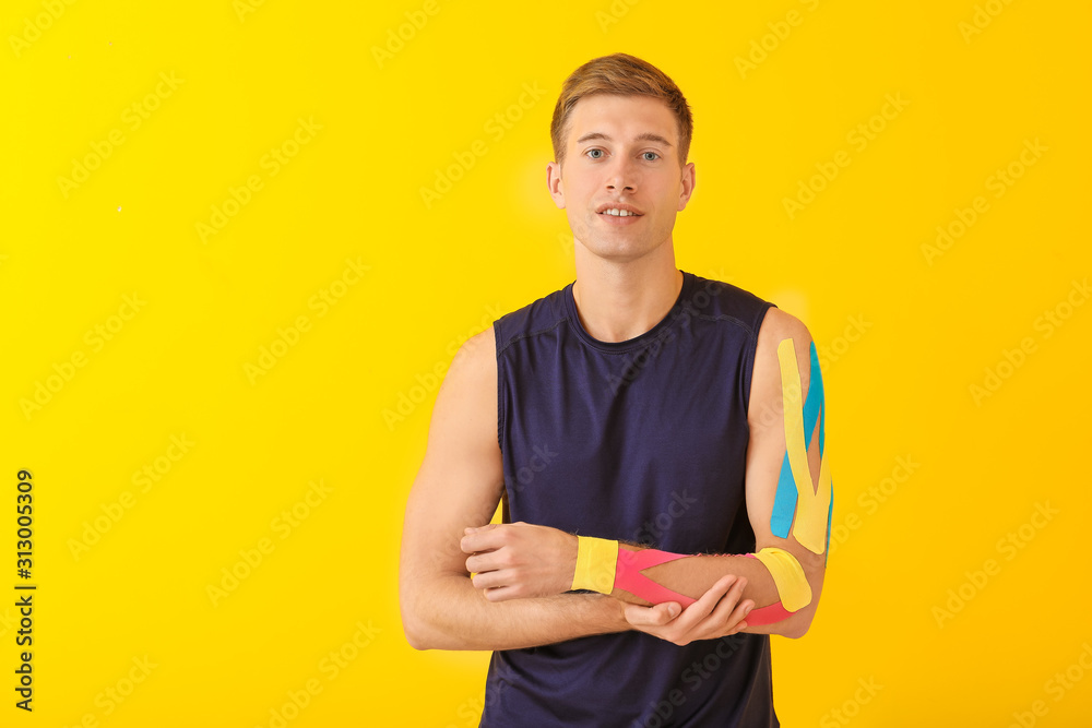 Sporty man with physio tape applied on arm against color background Sporty man with physio tape applied on arm against color background