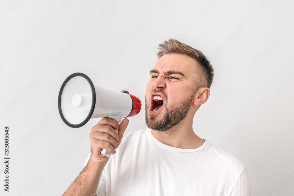 Emotional young man with megaphone on light background Emotional young man with megaphone on light background