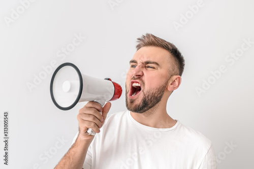 Emotional young man with megaphone on light background