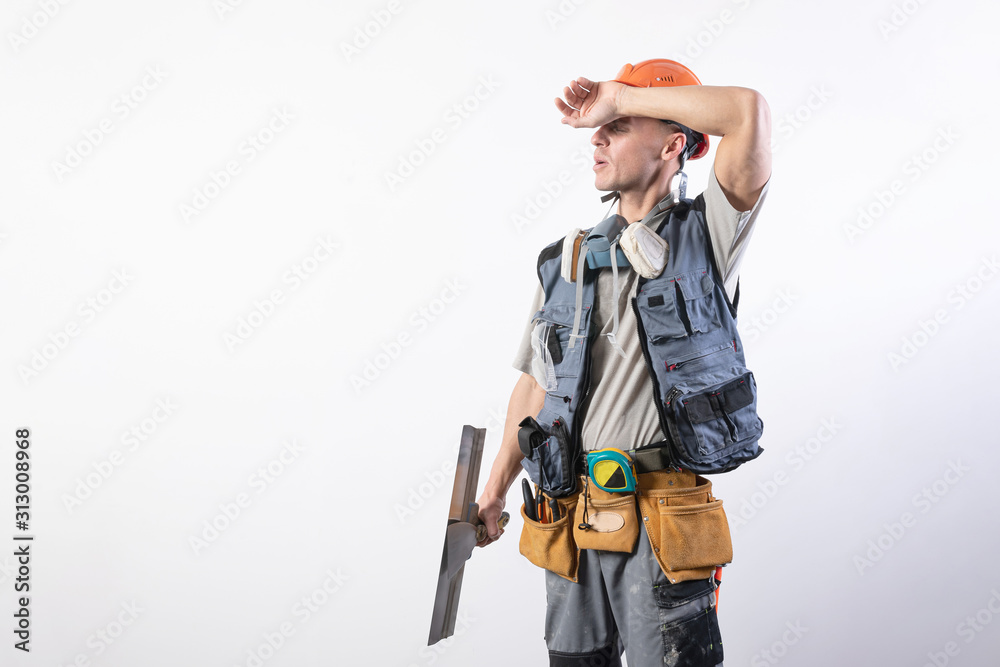 Tired builder with a spatula. In work clothes and hard hat. On a light gray background. Tired builder with a spatula. In work clothes and hard hat. On a light gray background.