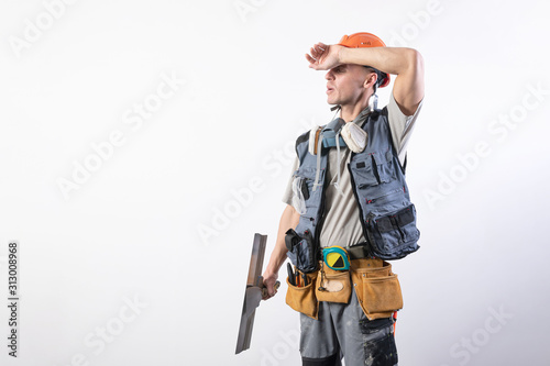 Tired builder with a spatula. In work clothes and hard hat. On a light gray background.