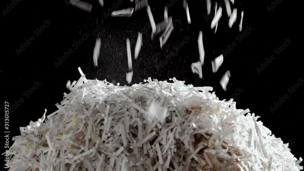 Shredded secret documents falling through the frame onto a pile of shredded paper against a black background.