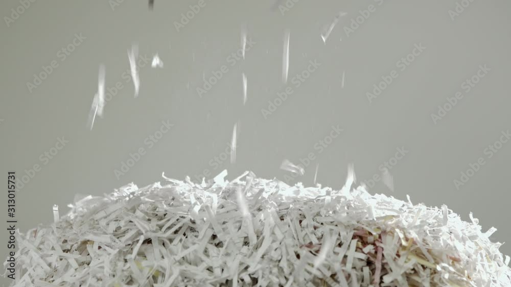 Shredded secret documents falling through the frame onto a pile of shredded paper against a white background.