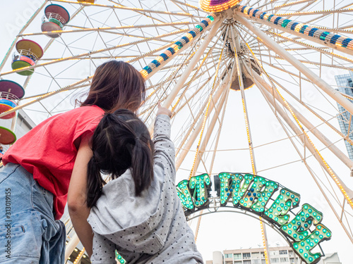 happy asia mother and daughter have fun in amusement carnival park with farris wheel and carousel background