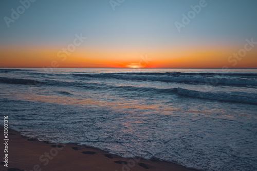 Fototapeta Naklejka Na Ścianę i Meble -  Abstract seascape. Beautiful tropical beach at sunset. Blue ocean, colorful sky, and sun setting down the horizon