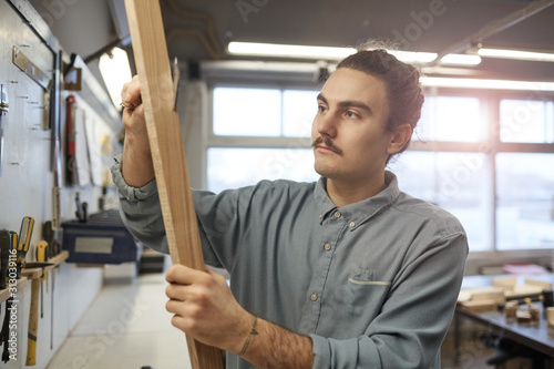 Young man Holding wooden plank and carving from the wood while working in workshop