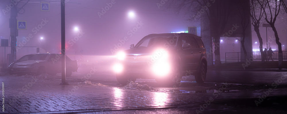 Obraz premium the car headlights through the fog, poor and dangerous driving conditions, night time in the city