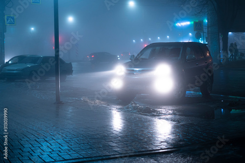 the car headlights through the fog, poor and dangerous driving conditions, night time in the city