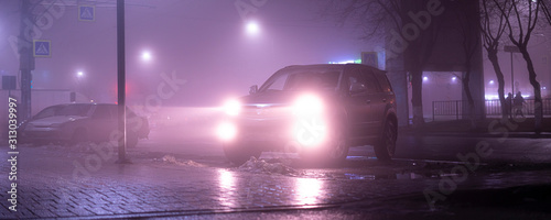 Fototapeta Naklejka Na Ścianę i Meble -  the car headlights through the fog, poor and dangerous driving conditions, night time in the city