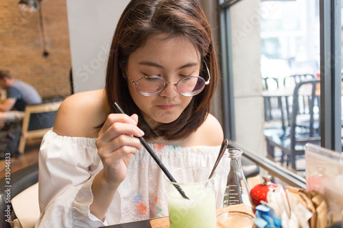 asian woman who wear glasses is stiring iced green beverage on glass photo