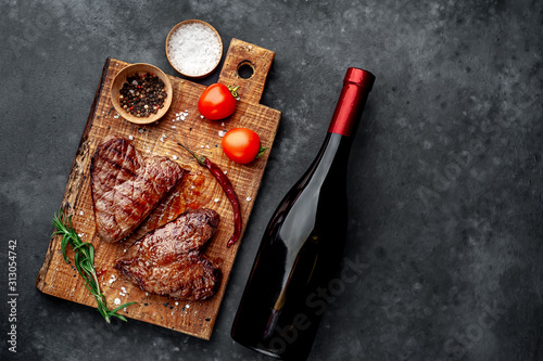two grilled beef steaks in the form of a heart with spices and a bottle of wine for dinner for Valentine's day on a stone background with copy space for your text