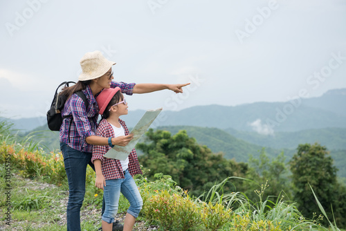 Mother and daughter stand on the mountain, pointing their hands forward. With a backpack and wearing a hat, standing, checking the map, with mountains in the background. Travel and adventure concepts