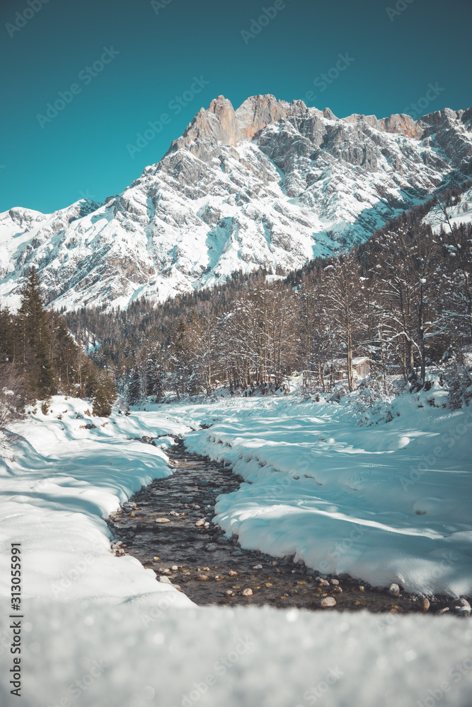 Sunny winter landscape in the alps: Mountain range, river, snowy trees, sunshine and blue sky
