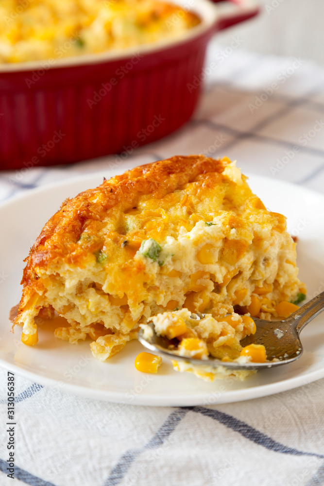 Homemade Cheddar Corn Pudding Casserole on a white plate, side view. Close-up. Homemade Cheddar Corn Pudding Casserole on a white plate, side view. Close-up.