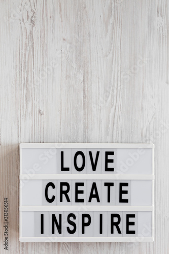 'Love create inspire' words on a lightbox on a white wooden surface, top view. Overhead, from above, flat lay. Copy space.