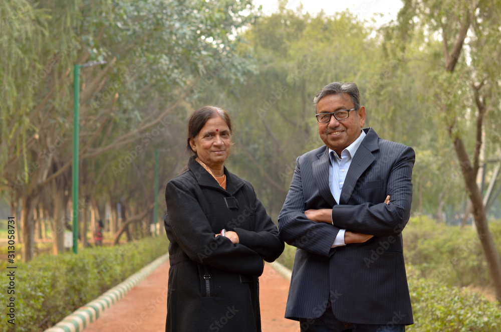 Portrait of a happy looking retired senior Indian man and woman couple smiling and posing with hands crossed / folded in a park outdoor during spring/summer season in Delhi, India. Concept love Portrait of a happy looking retired senior Indian man and woman couple smiling and posing with hands crossed / folded in a park outdoor during spring/summer season in Delhi, India. Concept love