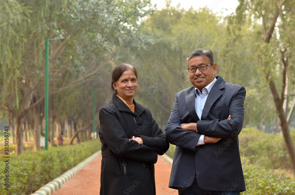 Portrait of a happy looking retired senior Indian man and woman couple smiling and posing with hands crossed / folded in a park outdoor during spring/summer season in Delhi, India. Concept love Portrait of a happy looking retired senior Indian man and woman couple smiling and posing with hands crossed / folded in a park outdoor during spring/summer season in Delhi, India. Concept love