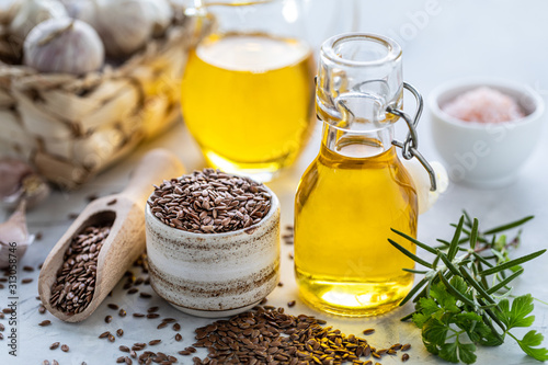 Fotografie Flaxseed oil in a bottle and ceramic bowl with brown flax seeds and wooden spoon on a white background