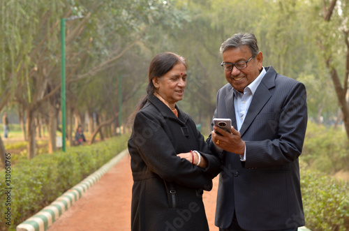 Senior Indian Bengali couple in park looking at their smart phone and smiling in a park in winters in New Delhi, India. Concept love
