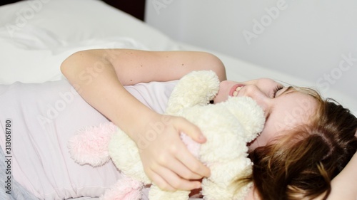 White Caucasian young girl (child, kid) smiling and relaxing lying in bed. lifestyle concept.