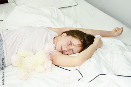 White Caucasian young girl (child, kid) lying on bed, stretch and relax in the morning. Lifestyle concept.