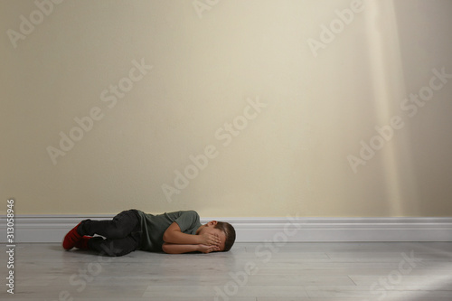 Little boy closing face with hands lying on floor near yellow wall, space for text. Child in danger © New Africa