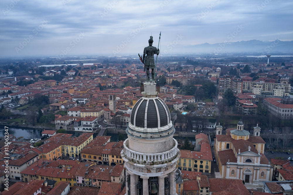 Foto Stock Panoramic aerial view of Torre Del Popolo a symbol of the city  of Palazzolo sull'Oglio, Italy. Statue of San Fedele. Low clouds, mountains  in the snow. Winter season. Aerial photography