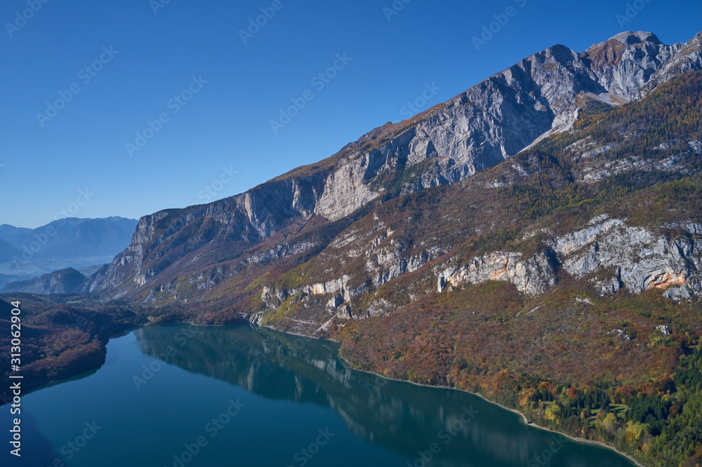 Aerial view of Lake Molveno, north of Italy. In the background rocky alps, blue sky. Reflection of mountains in water. Autumn season. Multi-colored palette of colors