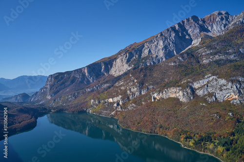 Fototapeta Naklejka Na Ścianę i Meble -  Aerial view of Lake Molveno, north of Italy. In the background rocky alps, blue sky. Reflection of mountains in water. Autumn season. Multi-colored palette of colors