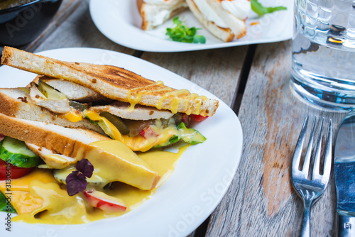 Classic breakfast, hot sandwiches with cheese, vegetables and chicken on a wooden table. Hand-made, rustic breakfast, toast with turkey and vegetables. Soft focus.