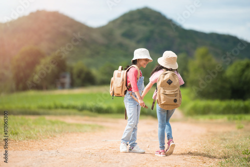 Two children carrying a backpack in the back and wearing a hat for a walk on a country road. She walked and enjoyed the surrounding nature. She enjoys traveling during the summer.