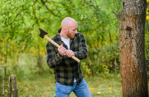 brutal and attractive male in forest. power and strength. lumberjack carry ax. bald woodsman worker. live on rancho. concept of masculinity. bearded hipster cut tree. man checkered shirt use axe