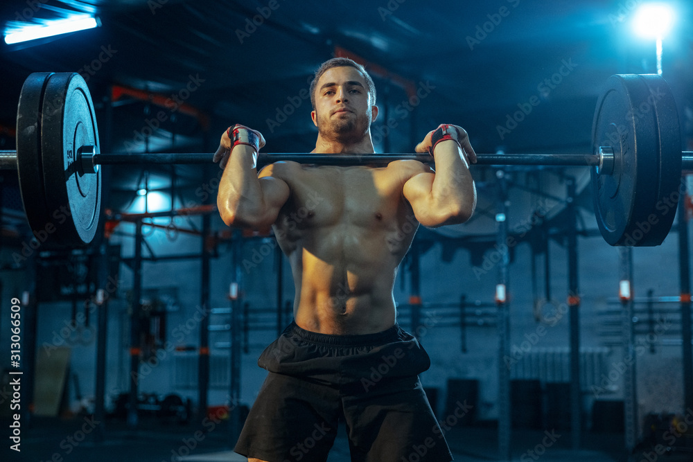 Caucasian man practicing in weightlifting in gym. Caucasian male sportive model training with barbell, looks confident and strong. Body building, healthy lifestyle, movement, activity, action concept. - obrazy, fototapety, plakaty 