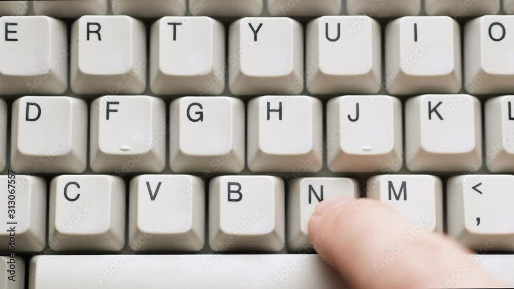 Male finger pushes N button on white keyboard. Slow motion and macro view