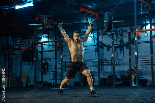Caucasian man practicing in weightlifting in gym. Caucasian male sportive model training with barbell  looks confident and strong. Body building  healthy lifestyle  movement  activity  action concept.