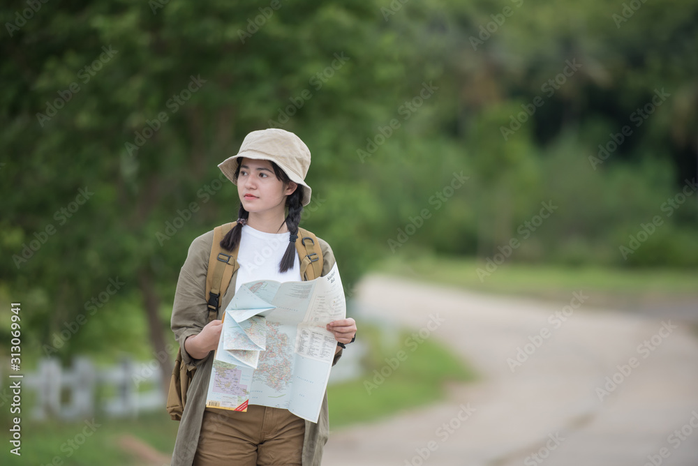 Happy asian woman girl goes to summer travel trip with mountain background. She traveled alone with a backpack checks map to find directions. Travel and adventure concept.