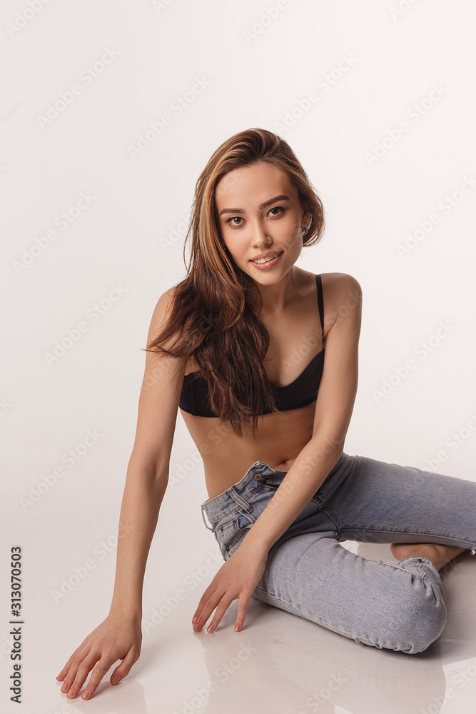 portrait of sexy smiling asian woman with long hair posing in black  lingerie, blue jeans on