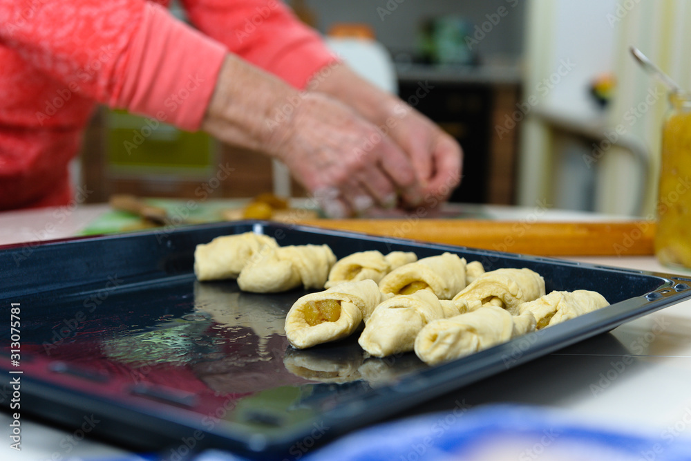 An old woman (80 years old) cooks at home in the kitchen, makes homemade cookies. Close-up, sharpness on a baking sheet with cookies.