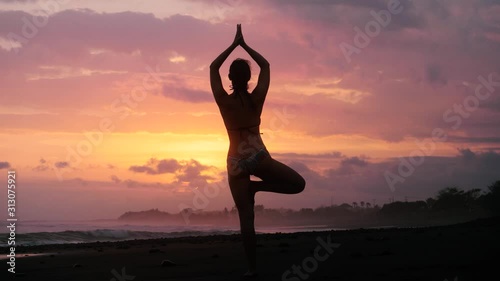 SLOW MOTION Young woman yoga pose practice at sunset on a tropical beach in bikini