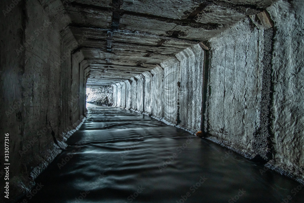 Light at the end of a turn in a square concrete rainwater or drain tunnel.