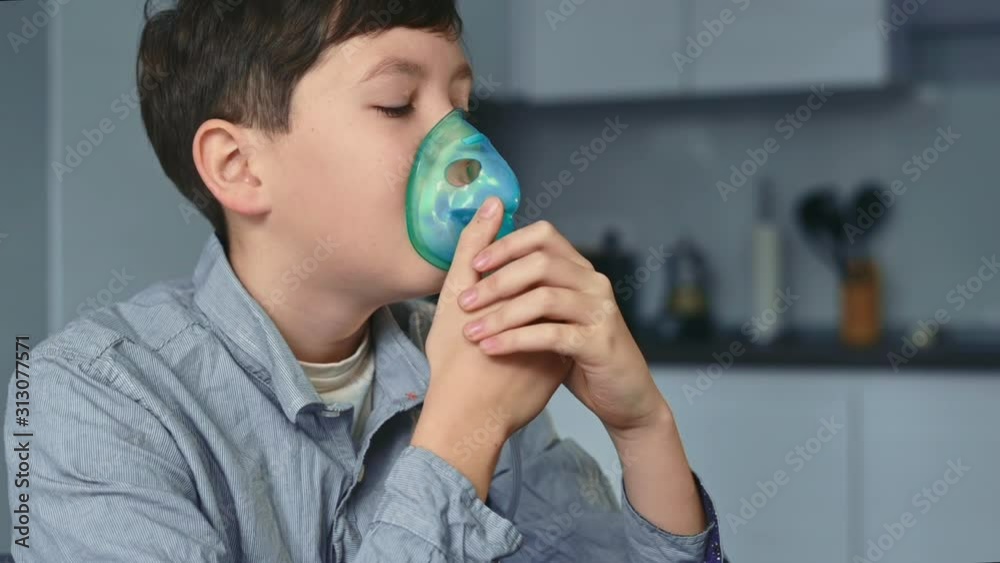 Treatment for asthma, the boy breathes through an inhaler. Standing in the kitchen Treatment for asthma, the boy breathes through an inhaler. Standing in the kitchen