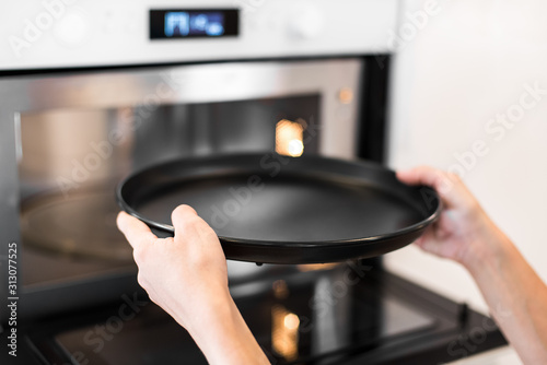 Girl puts a black baking dish in the oven in the kitchen