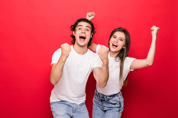 Photo of cheerful couple of two people rejoicing with victory of something while wearing white t-shirts with red background