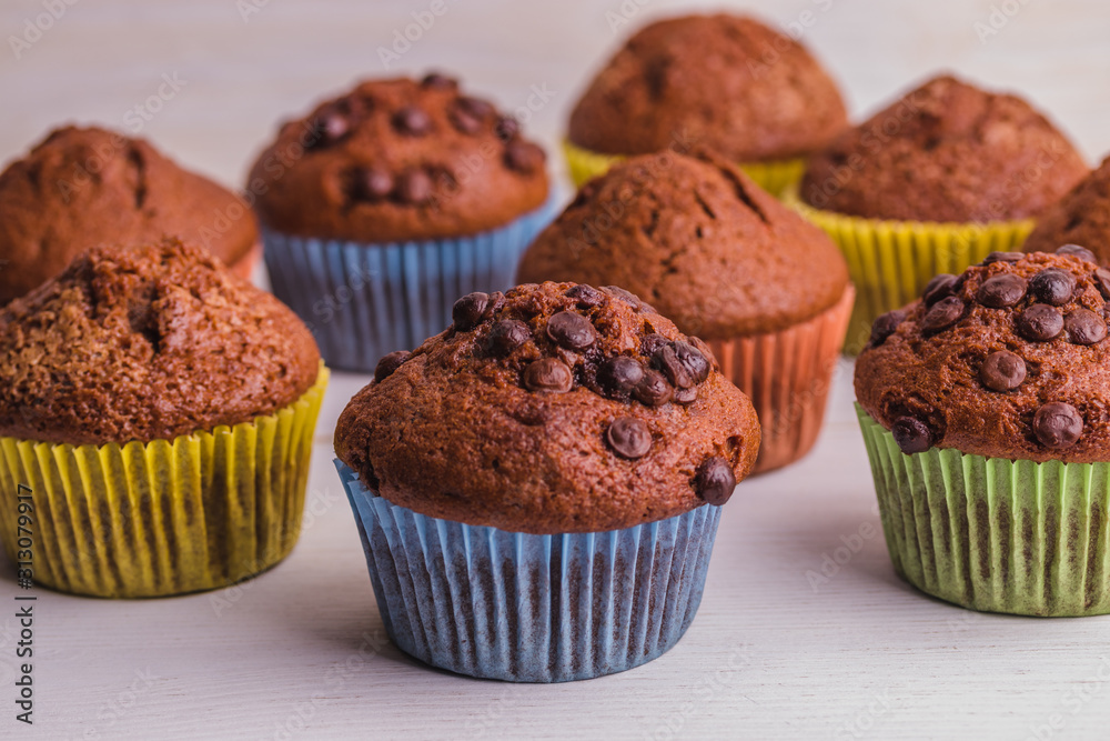 A few chocolate-sprinkled muffins in colored cups on a white wooden surface. A few chocolate-sprinkled muffins in colored cups on a white wooden surface.
