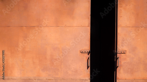 Sunlight on surface of the old metal sliding gate door of warehouse in brown rust proof paint was left ajar 