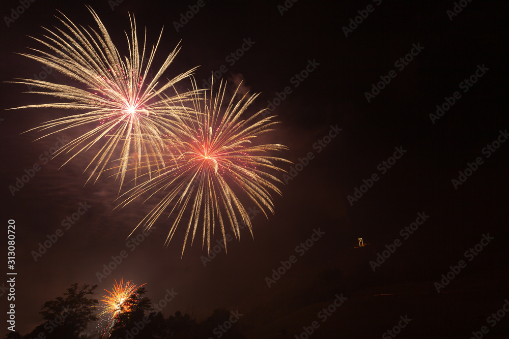 Bright orange and red fireworks over trees silhouette and over an illuminated church, Vittorio Veneto, Italy