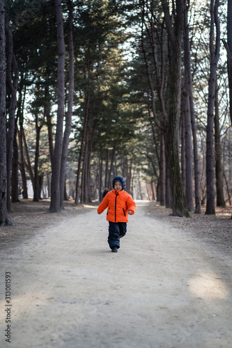 a happy boy is running with a winter suit in the forest.