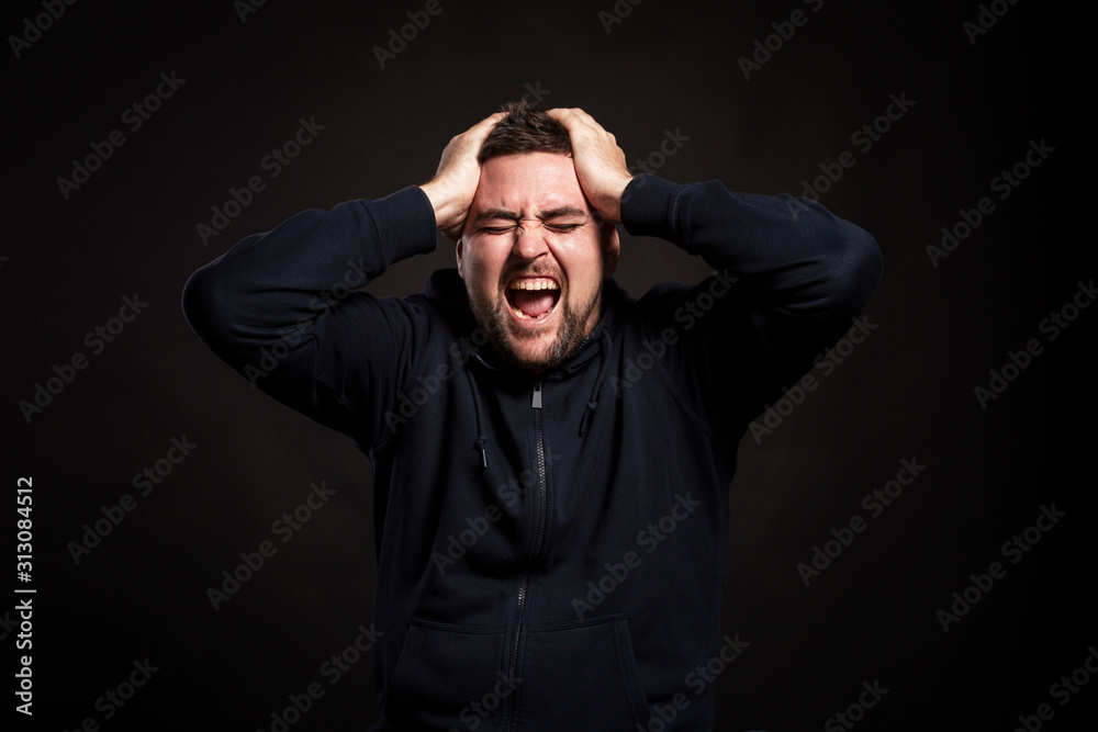 A man screams with his head in his hands. Depression and hopelessness. Black background. Close-up. A man screams with his head in his hands. Depression and hopelessness. Black background. Close-up.