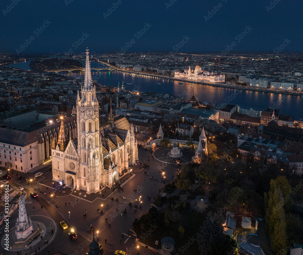 Naklejka premium Budapest, Hungary - Aerial drone view of the beautiful illuminated Matthias Church at blue hour with Fisherman's Bastion (Halaszbastya), Margaret Bridge and Parliament of Hungary at background